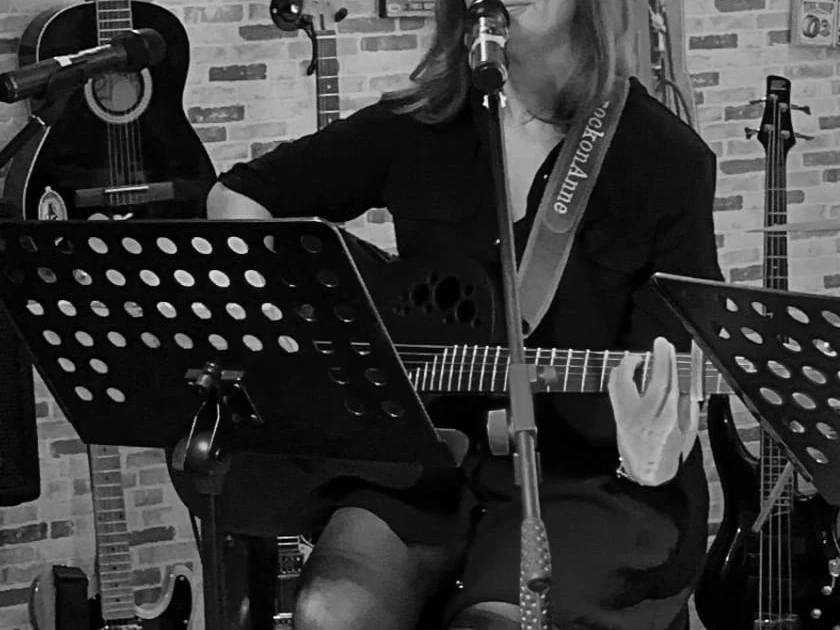 Musikerin.jpg Fünf Männer stehen nebeneinander, vier halten Musikinstrumente: zwei E-Gitarren, einen E-Bass, ein Keyboard und ein Schlagzeug mit Sticks.