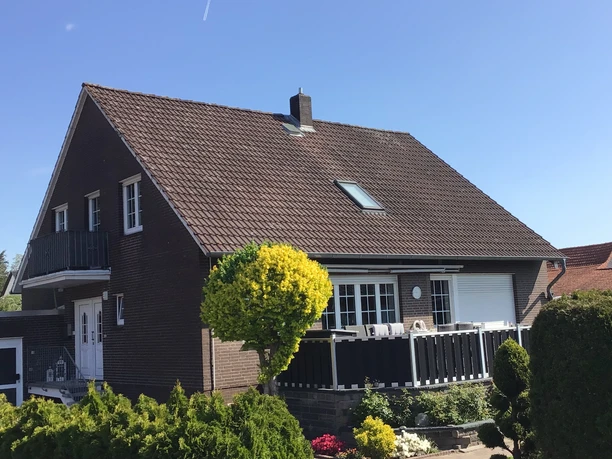 FeWo Kropp Zweistöckiges Backsteinhaus mit Balkon und Garten unter klarem blauem Himmel in ruhiger Vorstadtumgebung.