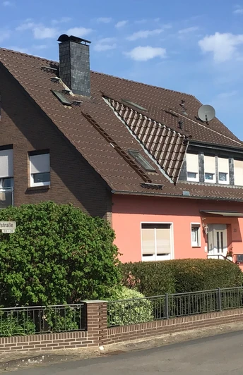 Ein zweistöckiges Haus mit roter Fassade und braunen Dächern, umgeben von grünen Büschen und Bäumen.A two-storey house with a red façade and brown roofs, surrounded by green bushes and trees.Et toetagers hus med rød facade og brune tage, omgivet af grønne buske og træer.Een huis van twee verdiepingen met een rode gevel en bruine daken, omringd door groene struiken en bomen.