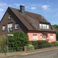 FeWo Süchting Ein zweistöckiges Haus mit roter Fassade und braunen Dächern, umgeben von grünen Büschen und Bäumen.