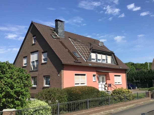 Een rood bakstenen huis van twee verdiepingen met een tuin staat onder een helderblauwe hemel.