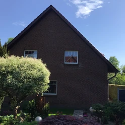 FeWo Brauer Backsteinhaus mit Steildach und gepflegtem Garten, diversen Pflanzen und einem kleinen Weg im Vordergrund.