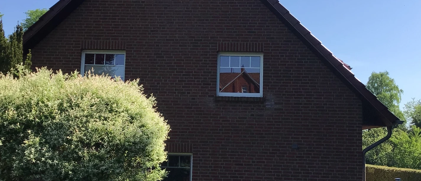 FeWo Brauer Backsteinhaus mit Steildach und gepflegtem Garten, diversen Pflanzen und einem kleinen Weg im Vordergrund.