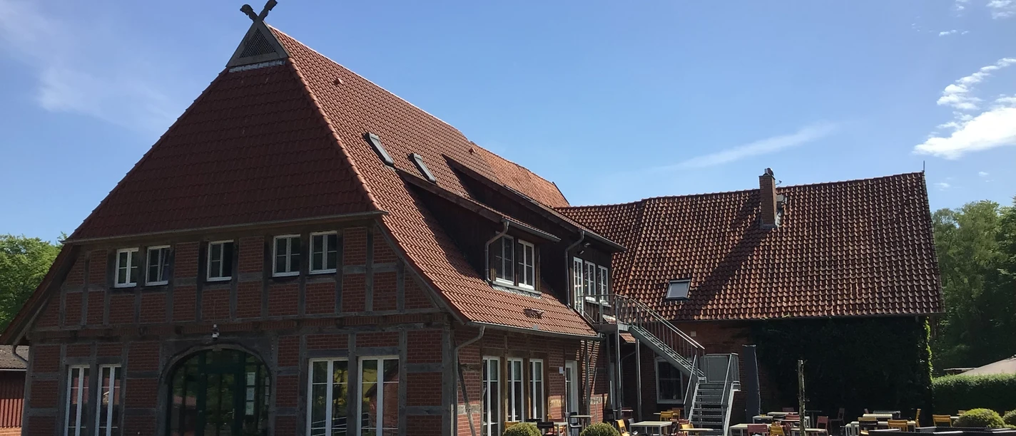 Een imposant bakstenen gebouw met rode dakpannen en een uitnodigend terras onder een blauwe hemel.