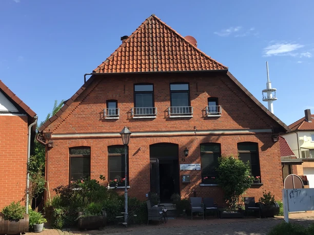Brick guest house with red roof tiles, green plants and a small entrance area.