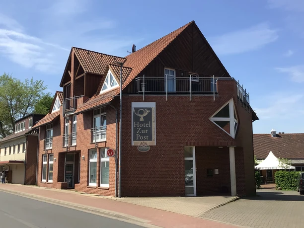 Een modern hotel met rode bakstenen en een opvallende gevel aan een rustige straat in de zon.