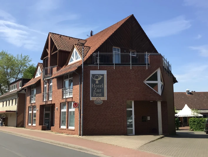 Hotel zur Post Ein modernes Hotel mit rotem Backstein und markantem Giebel an einer ruhigen Straße im Sonnenschein.