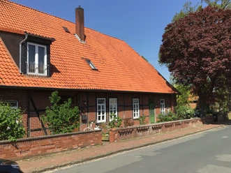 Ferienwohnung Runge Ein traditionelles rotes Ziegelhaus mit rotem Dach und Reet hinter einem gepflasterten Gehweg.