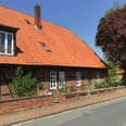 Ferienwohnung Runge Ein traditionelles rotes Ziegelhaus mit rotem Dach und Reet hinter einem gepflasterten Gehweg.