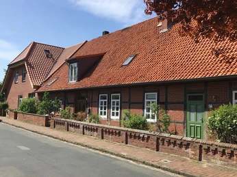 Ferienwohnung Runge Backsteinhaus mit roten Dachziegeln, grüner Tür und bunter Blumenrabatte entlang der Fassadenfront.Brick house with red roof tiles, green door and colorful flower border along the façade front.Murstenshus med røde tagsten, grøn dør og farverig blomsterkant langs facaden.Bakstenen huis met rode dakpannen, groene deur en kleurrijke bloemenrand langs de voorgevel.
