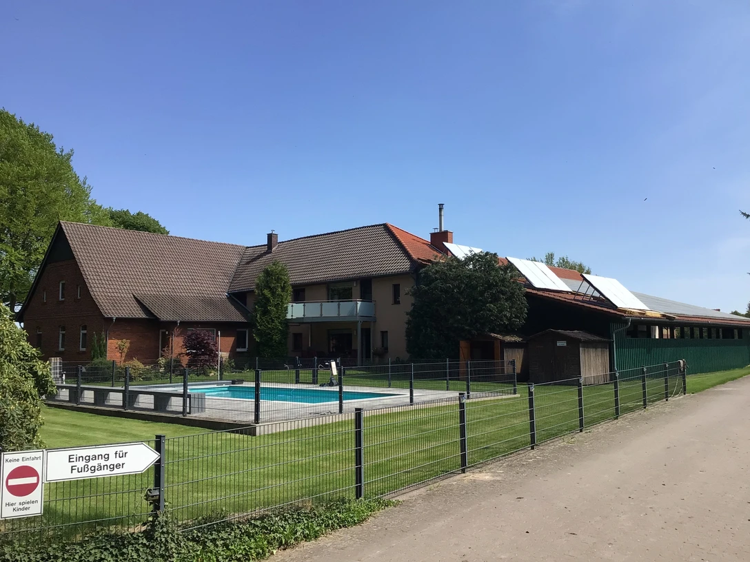 Ponyhof Hagedorn Ein Ponyhof mit mehreren Gebäuden, umzäuntem Außenbereich, Swimmingpool und Hinweisschild.