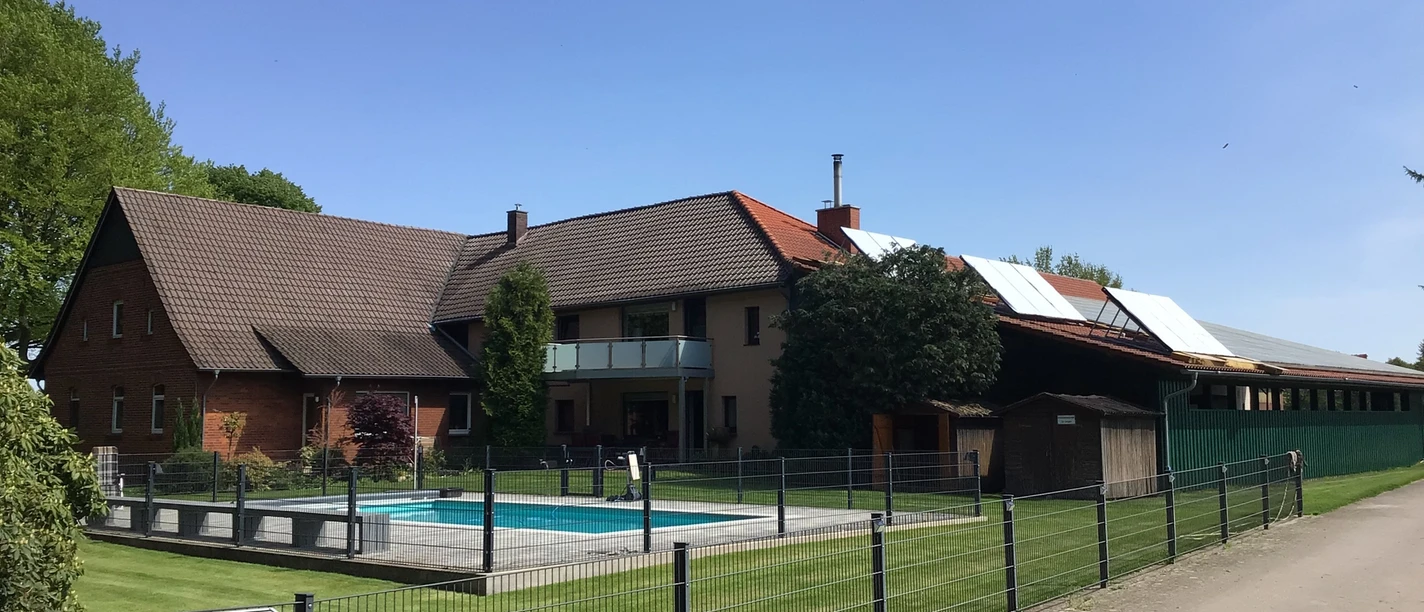 Ponyhof Hagedorn Ein Ponyhof mit mehreren Gebäuden, umzäuntem Außenbereich, Swimmingpool und Hinweisschild.