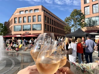 Feierabendmärkte Monheim am Rhein Mehrere Personen stoßen mit Weingläsern an einem belebten Markt auf einem sonnigen Platz an.