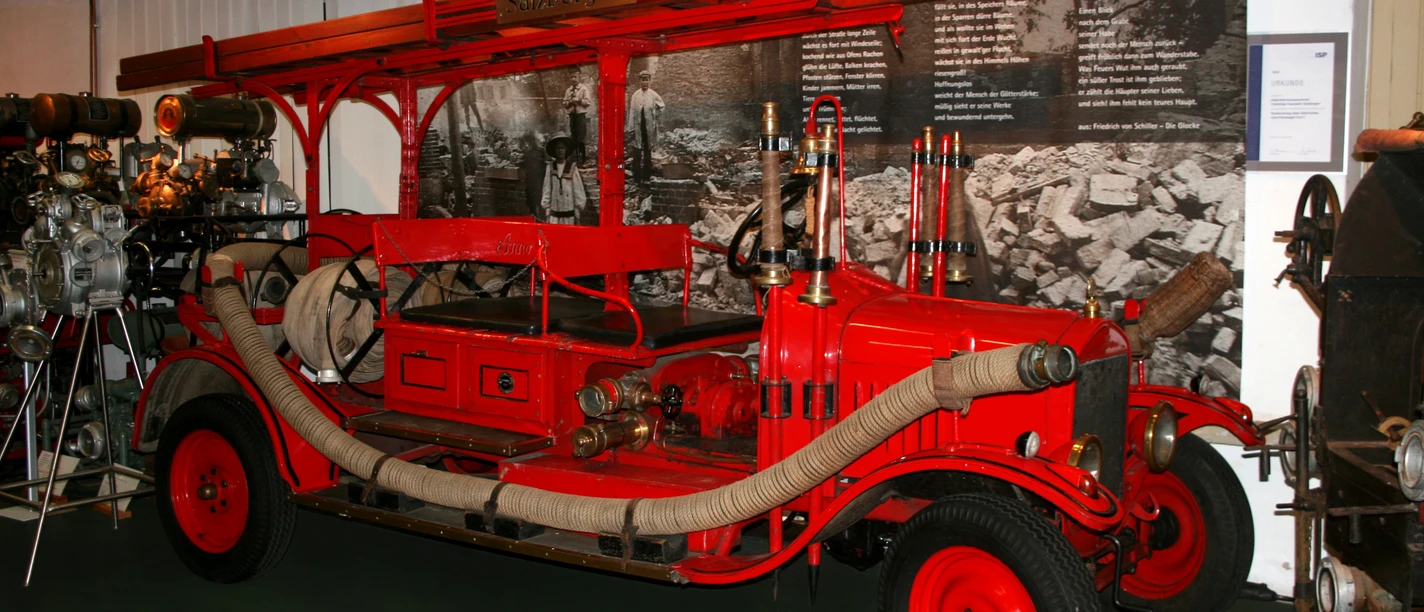 Feuerwehrmuseum Salzbergen.jpg Historische rote Feuerwehrspritze mit Schläuchen und Leitern im Ausstellungsraum des Museums.