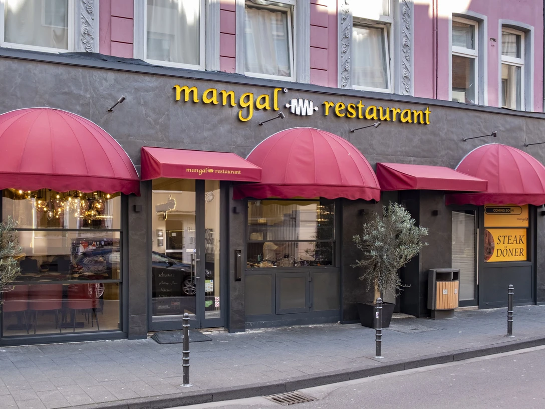 Mangal Restaurant Außenansicht mit rotem Vordach und eleganter Fassade in städtischer Umgebung.Exterior view with red canopy and elegant façade in an urban setting.