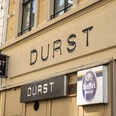 Durst Leuchtreklame „Durst“ auf Gebäudefront mit Gaffel Kölsch-Schild an einer historischen Straße.Illuminated sign reading ‘Durst’ (Thirst) on the front of a building with a Kölsch sign on a historic street.