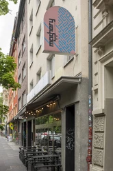 Mashery Hummus Kitchen Mashery Hummus Kitchen ist in einer belebten Kölner Straße gelegen. Außenansicht mit modernen Fassaden und einem markanten Logo zeigt den Eingang.