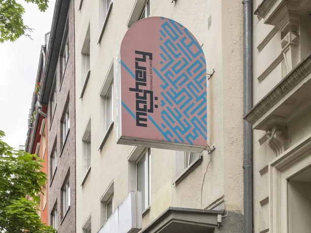 Mashery Hummus Kitchen Mashery Hummus Kitchen ist in einer belebten Kölner Straße gelegen. Außenansicht mit modernen Fassaden und einem markanten Logo zeigt den Eingang.