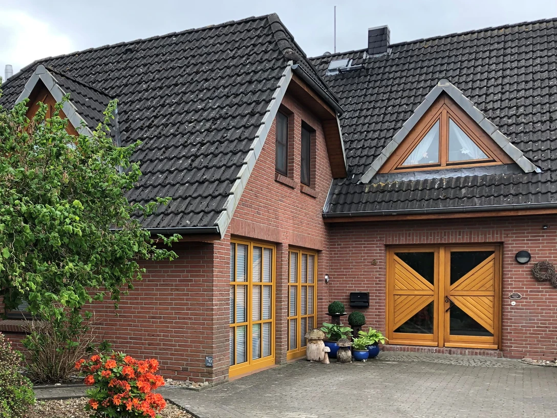 Filbry Ein rotes Backsteinhaus mit grauem Ziegeldach, großen hölzernen Türen und Fenstern, umgeben von Blumen.