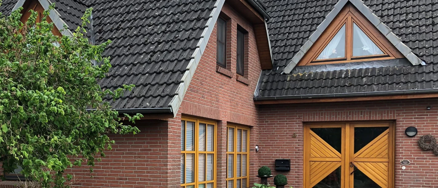 Filbry Ein rotes Backsteinhaus mit grauem Ziegeldach, großen hölzernen Türen und Fenstern, umgeben von Blumen.