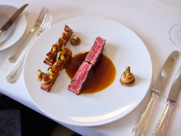 Altenberger Hof Gewagtes Gourmetgericht: Kunstvoll angerichtetes Fleisch mit Sauce, begleitet von Pilzen und Gemüseschnitten.