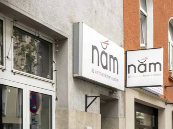 Nam La Vietnamienne Cuisine Außenansicht des vietnamesischen Restaurants "nâm" in einem Kölner Gebäude mit grauen Fassadenfliesen.Exterior view of the Vietnamese restaurant ‘nâm’ in a Cologne building with grey façade tiles.
