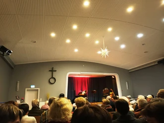 2025_Steterkult (1)_HD.jpg Publikum in einem Saal blickt auf eine Bühne mit roten Vorhängen und Musikinstrumenten.