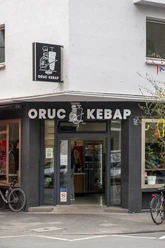Die Außenansicht von Oruc Kebap zeigt den Eingang des Restaurants mit einem klaren, schwarzen Schild über der Tür und zwei Fahrrädern, die neben dem Eingang an der Wand lehnen.