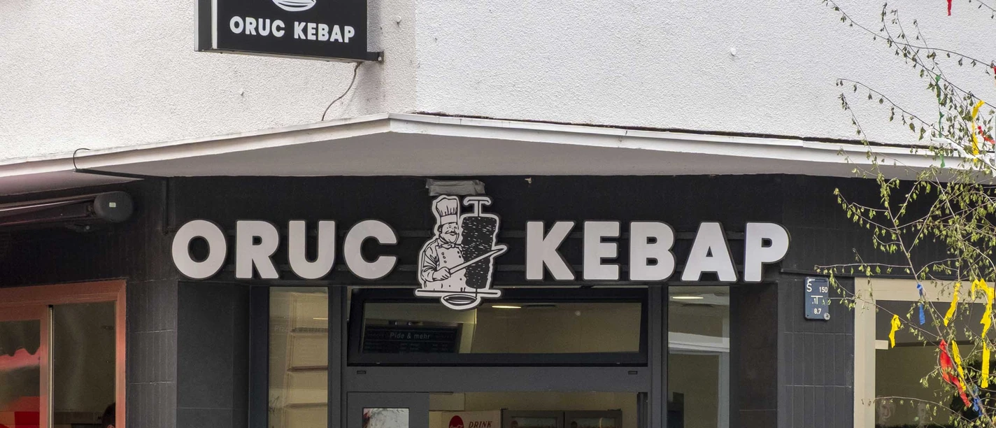 Die Außenansicht von Oruc Kebap zeigt den Eingang des Restaurants mit einem klaren, schwarzen Schild über der Tür und zwei Fahrrädern, die neben dem Eingang an der Wand lehnen.