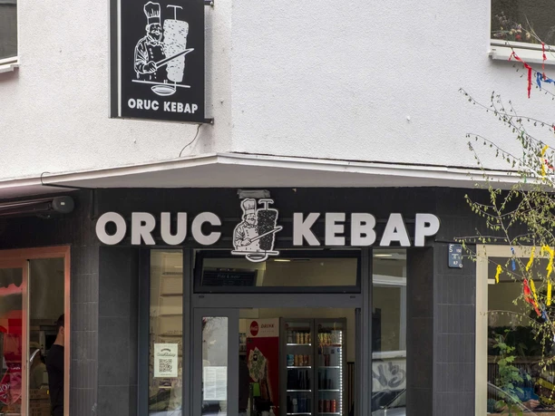 Oruc Kebap Die Außenansicht von Oruc Kebap zeigt den Eingang des Restaurants mit einem klaren, schwarzen Schild über der Tür und zwei Fahrrädern, die neben dem Eingang an der Wand lehnen.