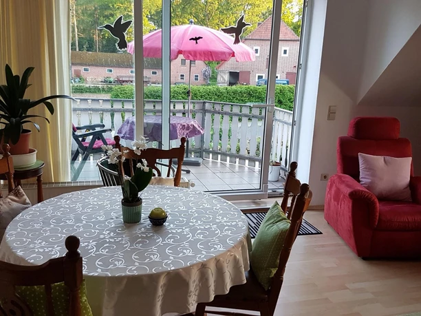 FeWo-Kühn-Wohnzimmer-3.JPG Runder Esstisch und roter Sessel in einem hellen Raum mit großer Fensterfront zum Balkon.