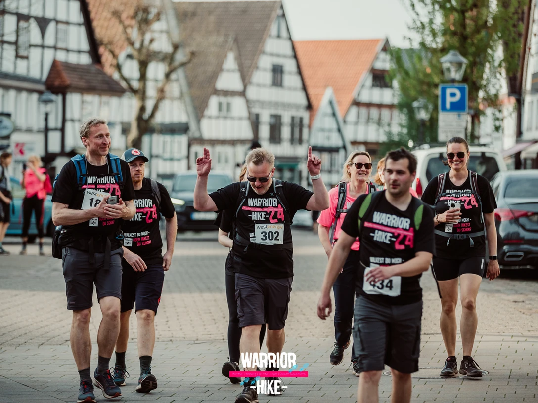 Teilnehmer einer Wanderveranstaltung in einem historischen Stadtzentrum mit Fachwerkhäusern und Zuschauer.