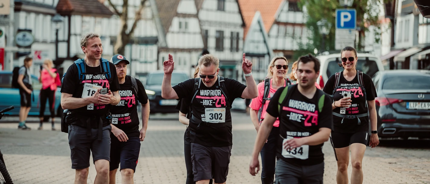 MAX_9531.jpg Teilnehmer einer Wanderveranstaltung in einem historischen Stadtzentrum mit Fachwerkhäusern und Zuschauer.