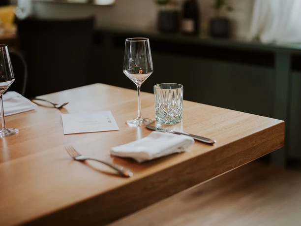 Restaurant Dreigang Herford- Lars May (3).jpg Ein stilvoll gedeckter Holztisch in einem Restaurant mit Gläsern, Besteck und einer Speisekarte.