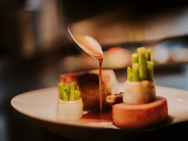 Fein angerichtetes Gericht mit grünem Spargel und Sauce auf einem Teller in einem gehobenen Restaurant.