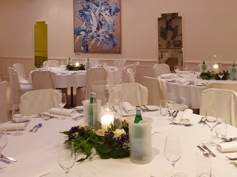 am-osterfeuer-5.jpg Ein festlich gedeckter Bankettsaal mit runden Tischen, Blumenarrangements und geschmackvoller Dekoration.