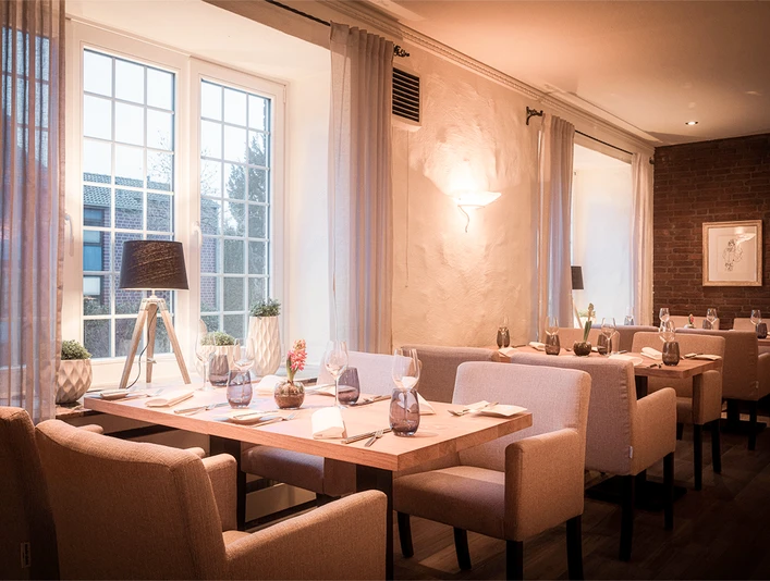 Ein stilvoll eingerichtetes Restaurant mit warmem Licht, gedeckten Tischen und großen Fenstern.