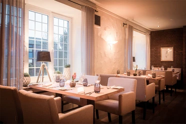 am-osterfeuer-8.jpg Ein stilvoll eingerichtetes Restaurant mit warmem Licht, gedeckten Tischen und großen Fenstern.