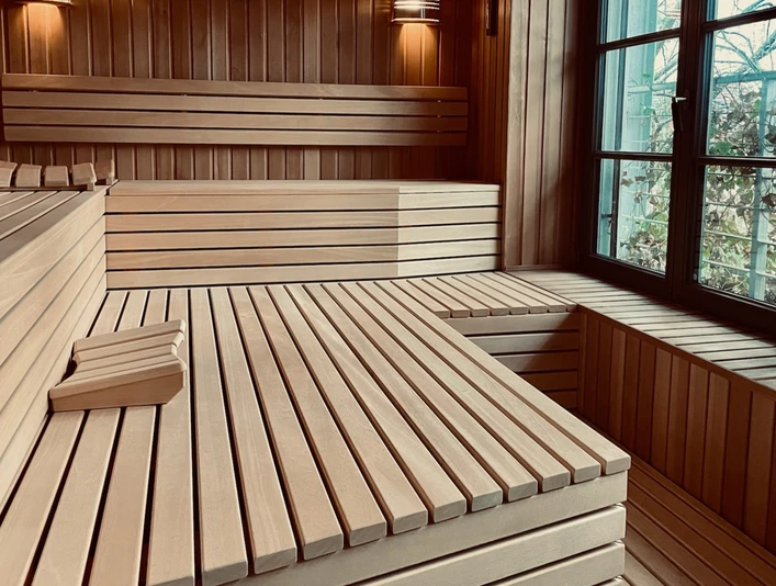 Sauna im Denkwerk Herford_Sauna.jpg Holzverkleidete Sauna mit großen Bänken, warmem Licht und einem Fenster mit Blick nach draußen.