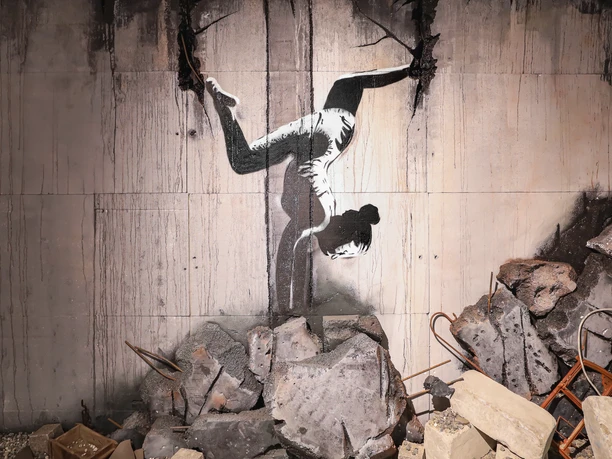 Turnerin in der Ukraine - House of Banksy Leipzig Bild aus der Ausstellung im House of Banksy in Leipzig von einem Graffiti einer Turnerin, die einen Handstand macht, das der Künstler in den Trümmern in der Ukraine gesprüht hat
