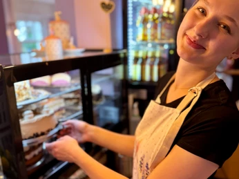 Café Clärchen in Velbert Freundliche Person hinterm Tresen eines Cafés mit einer Auswahl an Kuchen in der Auslage.
