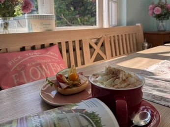 Café Clärchen in Velbert In einem lichtdurchfluteten Raum steht ein Holztisch mit einem belegten Bagel und einem Kakao mit Sahne.