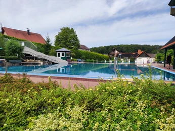 Waldfreibad Preußisch Oldendorf mit großer Wasserrutsche, umgeben von grüner Natur und blauen Himmel.