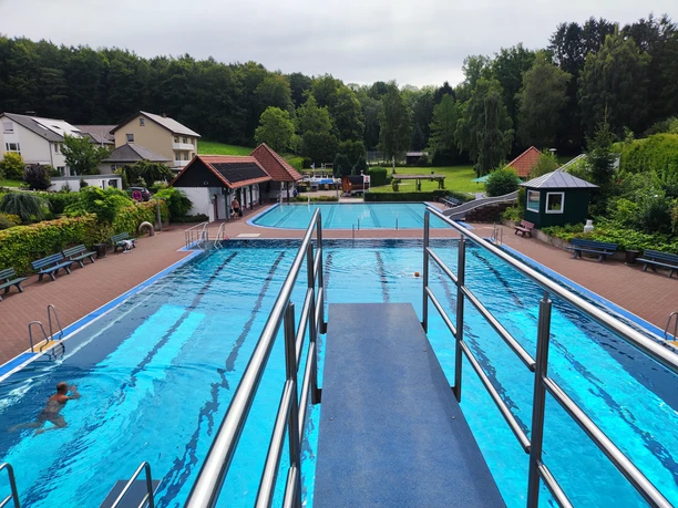 Waldfreibad Preußisch Oldendorf Außenansicht des Waldfreibads mit Schwimmbecken, Sprungturm, umgeben von Bäumen und Gebäuden.