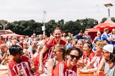 A smile lights up the face of a footballer in a red and white jersey, surrounded by a joyful group at the COME-TOGETHER-CUP in Cologne.