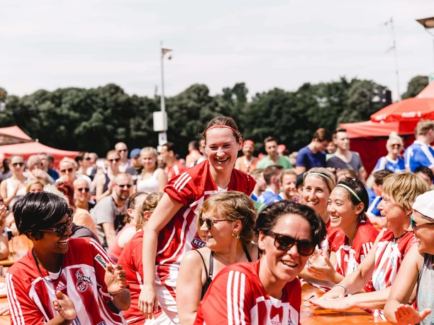 A smile lights up the face of a footballer in a red and white jersey, surrounded by a joyful group at the COME-TOGETHER-CUP in Cologne.