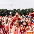 COME-TOGETHER-CUP-Koeln-Engel-Augenblicke.jpeg Ein Lächeln erhellt das Gesicht einer Fußballspielerin in einem rot-weißen Trikot, umgeben von einer freudigen Gruppe beim COME-TOGETHER-CUP in Köln.