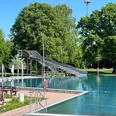 Freibad Achim Freibad mit großer Wasserrutsche im Grünen, umgeben von Bäumen und klarblauem Himmel.
