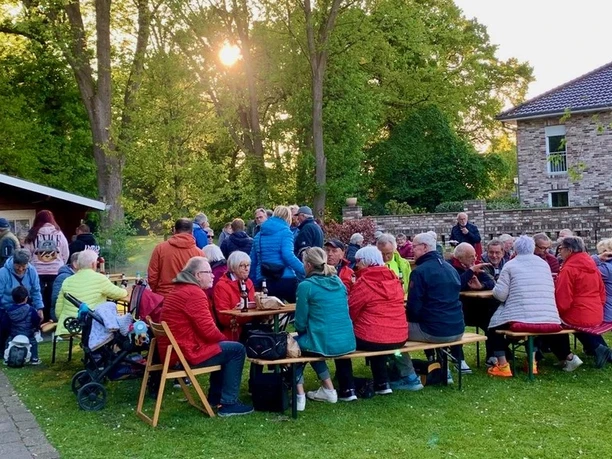 Grillen1.jpeg Eine große Gruppe von Menschen, teils in Rollstühlen, genießt im Freien ein geselliges Grillfest.