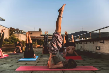 pexels-amin-sujan-529242-1375883.jpg Menschen üben auf Yoga-Matten im Freien den Schulterstand, umgeben von Natur und Abendstimmung.